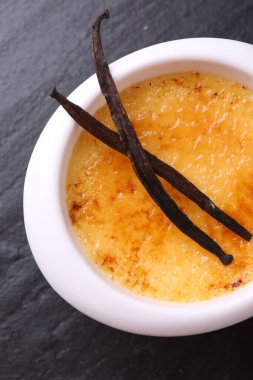 Lezzetli creme brulee kasede ve vanilyalı kaplar koyu gri desenli masa, üst manzara