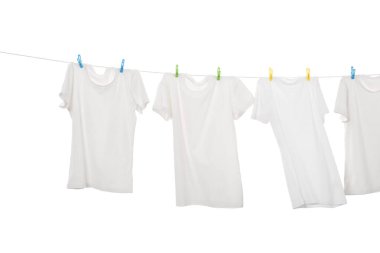 Çamaşır ipinde kuruyan birçok tişört beyaza izole edilmiş.