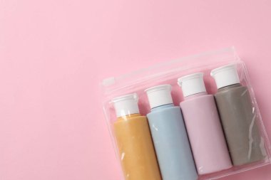 Pembe arka planda plastik poşet içinde kozmetik seyahat seti, üst manzara. Metin için boşluk