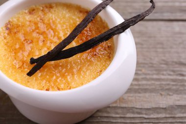 Lezzetli creme brulee kasede ve ahşap masada vanilya kabukları, yakın plan