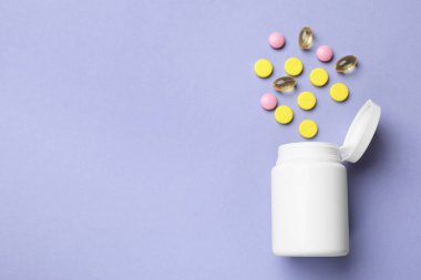 Beyaz şişe ve mor arka planda farklı vitamin hapları. Metin için boşluk