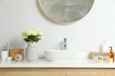 İçinde güzel beyaz güller ve banyo lavabosunun yanında tuvalet malzemeleri olan vazo.