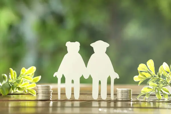 Pension savings. Figure of senior couple, stacked coins and green twigs on wooden table outdoors