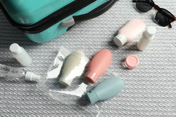 Cosmetic travel kit and plastic bag near suitcase on bed