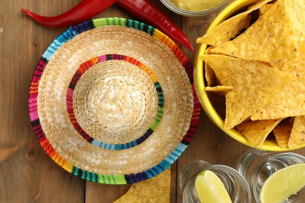 Mexican sombrero hat, tequila, nachos chips and chili peppers on wooden table, flat lay