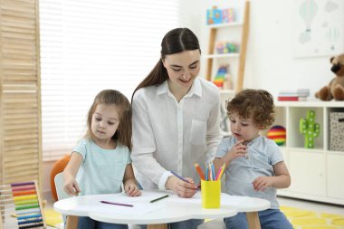 Anne ve küçük çocukları evde renkli kalemlerle resim yapıyorlar.