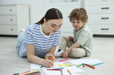Anne ve küçük oğlu evde renkli kalemlerle çizim yapıyorlar.