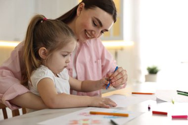 Anne ve küçük kızı mutfaktaki masada renkli kalemlerle resim çiziyorlar.