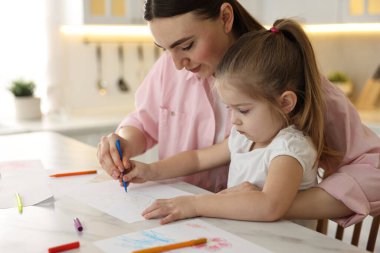 Anne ve küçük kızı mutfaktaki masada renkli kalemlerle resim çiziyorlar.