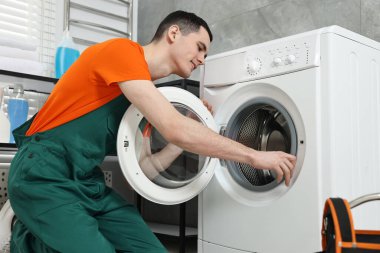 Gülümseyen tesisatçı banyoda çamaşır makinesini tamir ediyor.