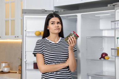 Mutfaktaki boş buzdolabının yanında turşu kavanozu olan üzgün bir kadın.