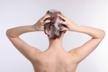Saçını şampuanla yıkayan genç bir kadın açık gri arka plan, arka görüş