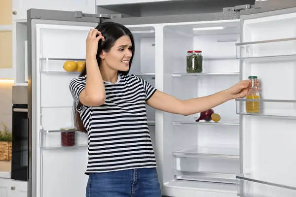Upset woman near empty refrigerator in kitchen