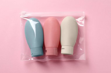 Pembe arka planda plastik poşet içinde kozmetik seyahat seti, üst manzara. Banyo aksesuarları