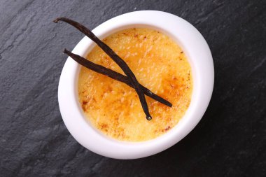 Lezzetli creme brulee kasede ve vanilyalı kaplar koyu gri desenli masa, üst manzara