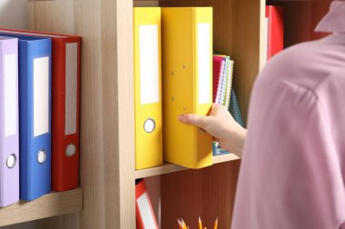 Kadın raflardan klasör ofis klasörünü alıyor, yakın plan.
