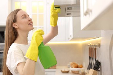 Evde sprey şişesi ve mikrofiber bez mutfak kaputu temizleyen bir kadın var.