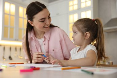Anne ve küçük kızı mutfaktaki masada renkli kalemlerle resim çiziyorlar.