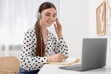 E-öğrenme. İçerideki masada online ders sırasında dizüstü bilgisayar kullanan genç bir kadın.