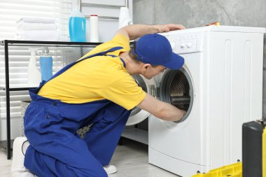 Genç tesisatçı banyoda çamaşır makinesini tamir ediyor.