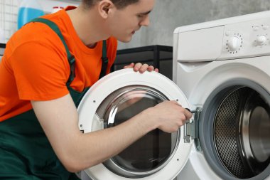 Genç tesisatçı banyoda çamaşır makinesini tamir ediyor.