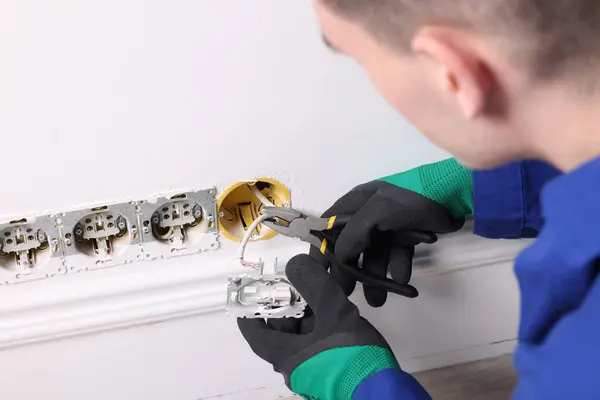 Professional repairman fixing power sockets with pliers indoors, closeup