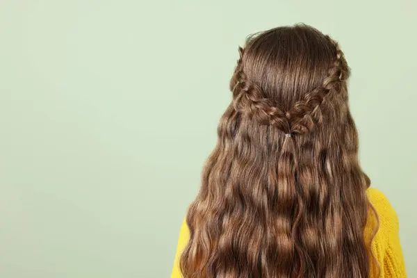 Little girl with braided hair on light green background, back view. Space for text