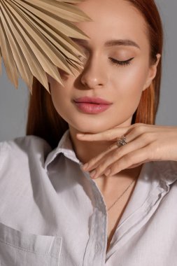 Gri arka planda dekoratif yaprağı olan güzel genç bir kadın.