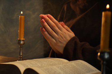 Masada yanan mumlar ve İncil 'le dua eden kadın, yakın plan.