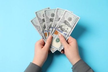 Para değişimi. Açık mavi zemin üzerinde dolar banknotları tutan kadın, üst görünüm