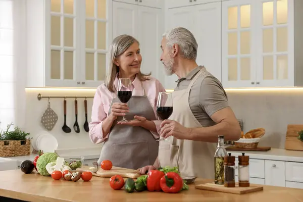 Happy senior couple with glasses of wine cooking together in kitchen