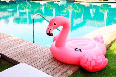 Lüks bir tatil köyünde yüzme havuzunun yanındaki tahta güvertede flamingo şeklinde süzül.