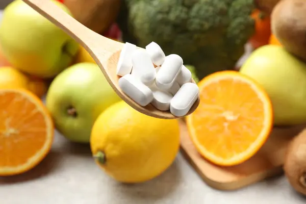 Dietary supplements. Spoon with pills over food products at grey table, closeup