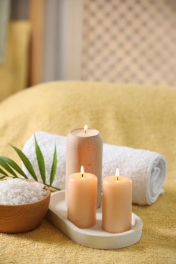 Spa kompozisyonu. Yumuşak sarı yüzeyde yanan mumlar, deniz tuzu ve havlu.
