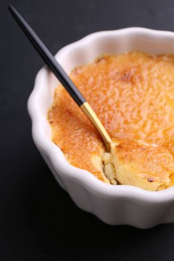 Koyu gri masada kaşık ve kâsede leziz krema brulee, yakın plan.