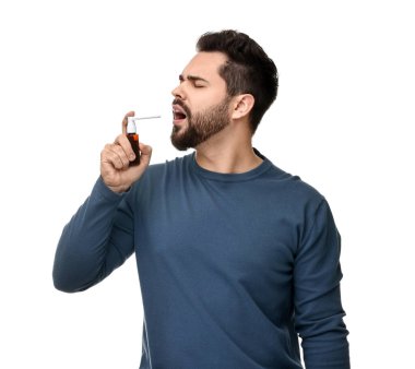 Genç adam beyaz arka planda boğaz spreyi kullanıyor.