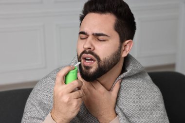 Genç adam evde boğaz spreyi kullanıyor.