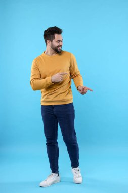 Mutlu genç adam açık mavi arka plandaki bir şeyi işaret ediyor.