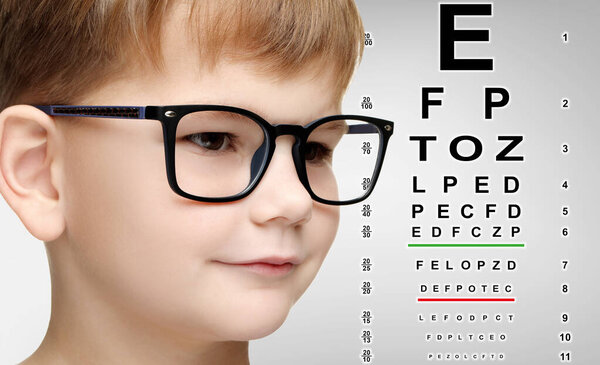 Vision test. Cute little boy in glasses and eye chart on light grey background