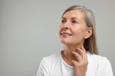 Gri arka planda boynuna dokunan güzel bir kadın, mesaj için boşluk