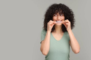 Dişlerinin beyazlatılması için gri arkaplan ve metin için alan kullanan genç bir kadın.