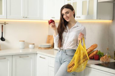 Mutfakta bir torba ekmek ve elma taşıyan bir kadın.