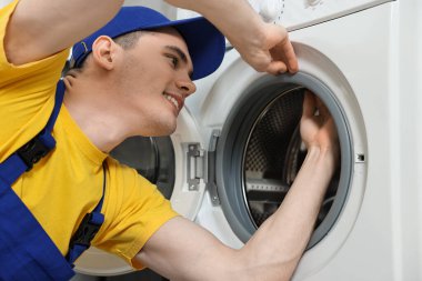 Gülümseyen tesisatçı çamaşır makinesinin kapısına bakıyor.