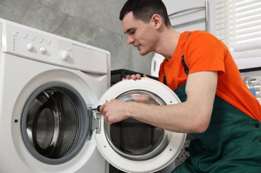 Gülümseyen tesisatçı banyoda çamaşır makinesini tamir ediyor.