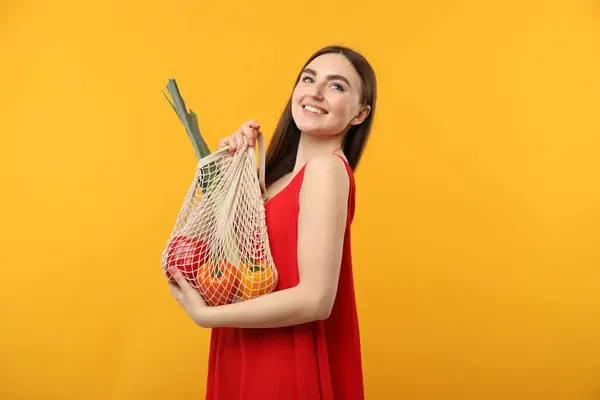 stock image Woman with string bag of fresh vegetables on orange background