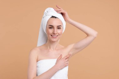 Güzel bir kadın bej arka planda pürüzsüz, temiz bir ciltle koltukaltı gösteriyor.