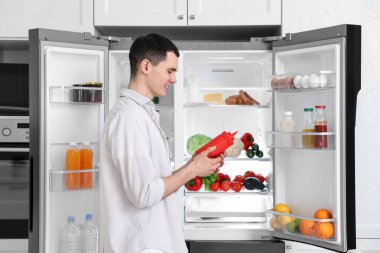 Mutfakta buzdolabının yanında ketçap tutan mutlu adam.