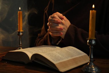 Masada yanan mumlar ve İncil 'le dua eden kadın, yakın plan.