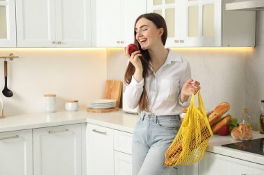 Mutfakta bir torba ekmek ve elma taşıyan bir kadın.