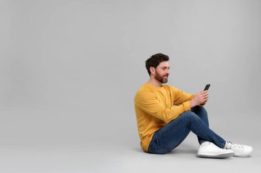 Gri arka planda akıllı telefonu olan gülümseyen bir adam. Metin için boşluk